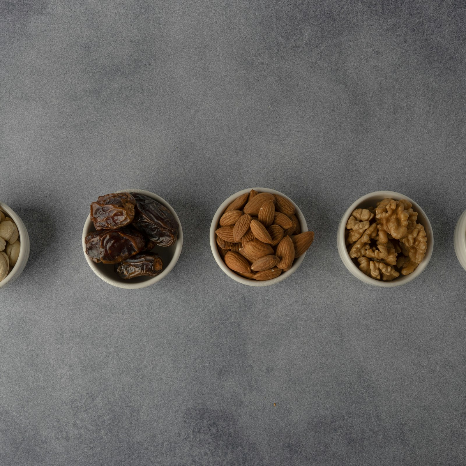 Ceramic bowls of cashews, dates, almonds and walnuts arranged on stone